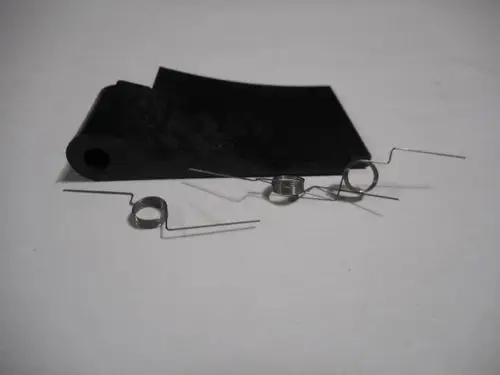 Schwarzes Gummimaterial mit zwei Spiralfedern und einem gebogenen Draht. Teile, die zu einer Luftklappe von Remeha gehören, liegen auf einer hellen Oberfläche.